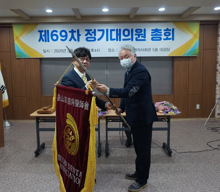 한상욱 부산지부 신임 회장 당선자(사진 왼쪽)가 배종현 회장으로부터 ‘부산광역시치과의사회기’를 전달 받고 있다.<부산지부 제공>